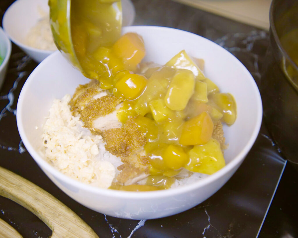 pouring curry over katsu chicken and white rice